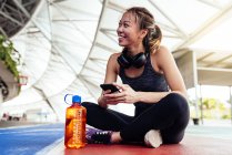 Азиатская женщина в фитнес носить с помощью смартфона, сидя — стоковое фото