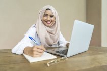 Joven asiático musulmán mujer utilizando portátil en el interior - foto de stock