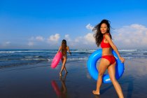 Two pretty girls with floaties on the way to the waves of the ocean. One girl is turning around smiling. — Stock Photo