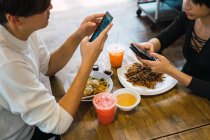 Joven asiático pareja usando smartphones en café - foto de stock
