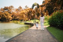 Cute asian mother and daughter walking near water in park — Stock Photo