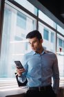 Homem de negócios adulto jovem usando smartphone no escritório moderno — Fotografia de Stock