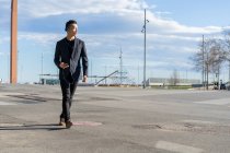 Молодий азіатський чоловік з гарнітурою, що йде в місті — стокове фото
