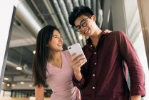 Jovem asiático bem sucedido casal de negócios compartilhamento smartphone no escritório moderno — Fotografia de Stock