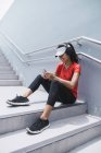 Young asian sporty woman using headphones and smart on stairs — Stock Photo