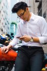 Successful young businessman using smartphone and sitting on bike — Stock Photo