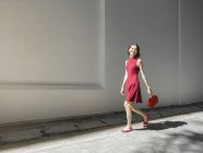 Mulher chinesa andando contra a parede branca com bolsa — Fotografia de Stock