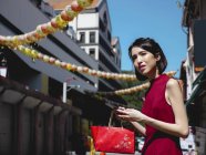 Mujer china usando teléfono inteligente y cartera de espera - foto de stock