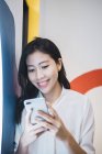 Молодая азиатка, использующая смартфон в креативном современном офисе — стоковое фото
