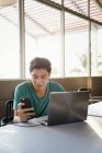 Молодий привабливий азіатський чоловік використовує смартфон і ноутбук в кафе — стокове фото