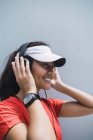 Молода азіатська спортивна жінка використовує навушники на сірому фоні — стокове фото
