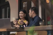 Happy young asian couple using smartphone in cafe — Stock Photo