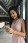 Молода азіатська успішна бізнес-леді зі смартфоном в сучасному офісі — стокове фото