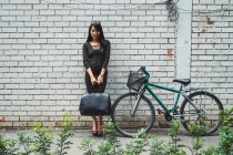 Joven asiático mujer de pie con bolsa al lado de bicicleta - foto de stock