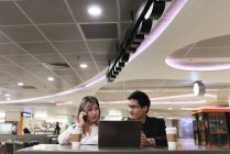 Young asian couple of businesspeople using digital devices in airport — Stock Photo