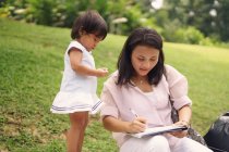 Cute asian mother and daughter making notes in park — Stock Photo
