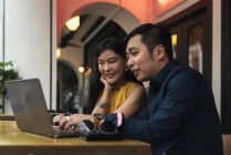 Feliz joven asiático pareja usando laptop en café - foto de stock