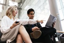 Молодая азиатская пара бизнесменов в аэропорту, женщина указывает на ноутбук — стоковое фото