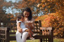 Cute asian mother and daughter using smartphone on bench — Stock Photo