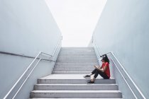 Вид сбоку на молодую женщину спортивного телосложения в наушниках и умную на лестнице — стоковое фото