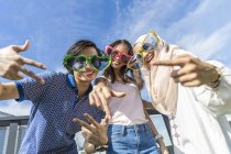 Grupo de amigos vestindo óculos engraçados se divertindo contra o céu azul — Fotografia de Stock