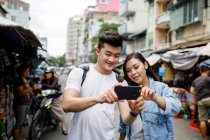 LIBERTAS Pareja asiática joven tomando selfie en un mercado local en Ho Chi Minh City, Vietnam - foto de stock
