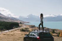 Young woman sitting on top of car in Milford Sound, New Zealand — Stock Photo