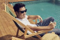 Feliz asiático homem em óculos de sol relaxante perto da piscina — Fotografia de Stock