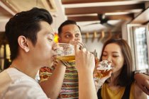 Young asian friends drinking beer together in bar — Stock Photo