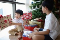 Азиатская семья празднует Рождество, мальчики распаковывают подарки — стоковое фото