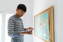 Giovane asiatico uomo a casa tenendo il suo taccuino accanto mappa — Foto stock
