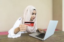 Joven asiático musulmán mujer usando portátil y celebración de tarjeta de crédito - foto de stock