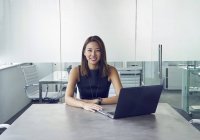 Молода азіатська бізнес-леді працює з ноутбуком в сучасному офісі — стокове фото