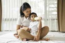 Азіатська мати дивиться, як її син харчується пляшкою молока — стокове фото