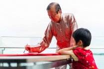 Дід з онуком малює ієрогліфи каліграфії — стокове фото
