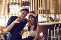 Felice giovani amici asiatici coppia Natale insieme nel caffè e prendendo selfie — Foto stock