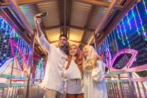 Tres jóvenes musulmanes se están tomando una selfie durante la noche en un puente - foto de stock
