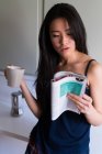 Jovem chinesa lendo uma revista com uma xícara de café dentro de casa — Fotografia de Stock