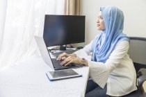 Молода азіатська мусульманка працює вдома з ноутбуком — стокове фото