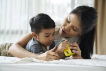 Asiática mãe e filho brincando com brinquedos na cama — Fotografia de Stock