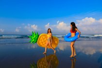 Two pretty girls with floaties on the way to the waves of the ocean. — Stock Photo