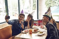 Happy young asian friends celebrating christmas together in cafe and taking selfie — Stock Photo