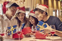 Happy young asian friends celebrating christmas together in cafe and sharing gifts — Stock Photo