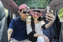 Junges Paar macht ein Selfie auf dem Rücksitz eines Autos — Stockfoto