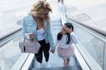 Glückliche junge Mutter mit ihrer Tochter im Gespräch auf der Rolltreppe in der Stadt. — Stockfoto