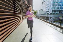 Une jeune femme asiatique fait du jogging dans la ville de Singapour tôt le matin. Elle passe une section d'architecture en acier et en verre . — Photo de stock