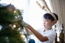 Happy asian boy decorating fir tree at home — Stock Photo
