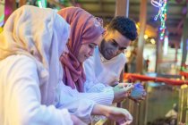 Три друга-мусульманина смотрят вниз на мобильный телефон на мосту ночью — стоковое фото