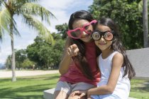 Joven asiático madre con lindo hija sentado en banco en divertido gafas - foto de stock
