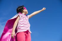 Милий маленький супергерой дівчинка в масці і пальто позує на небо — стокове фото